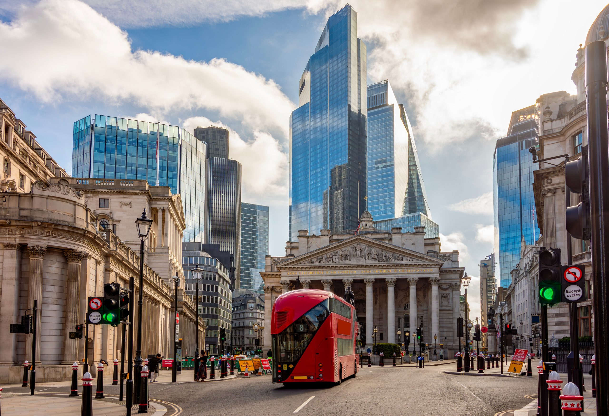 An iconic London view, with a red bus passing the Royal Exchange and glass skyscrapers in the background