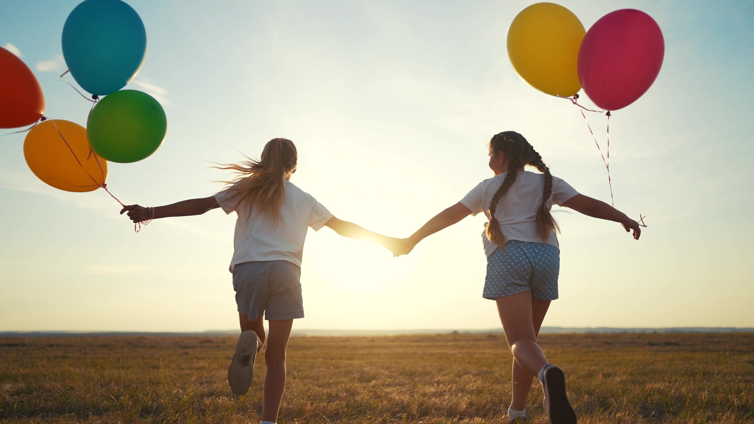 Children running towards a sunset with balloons