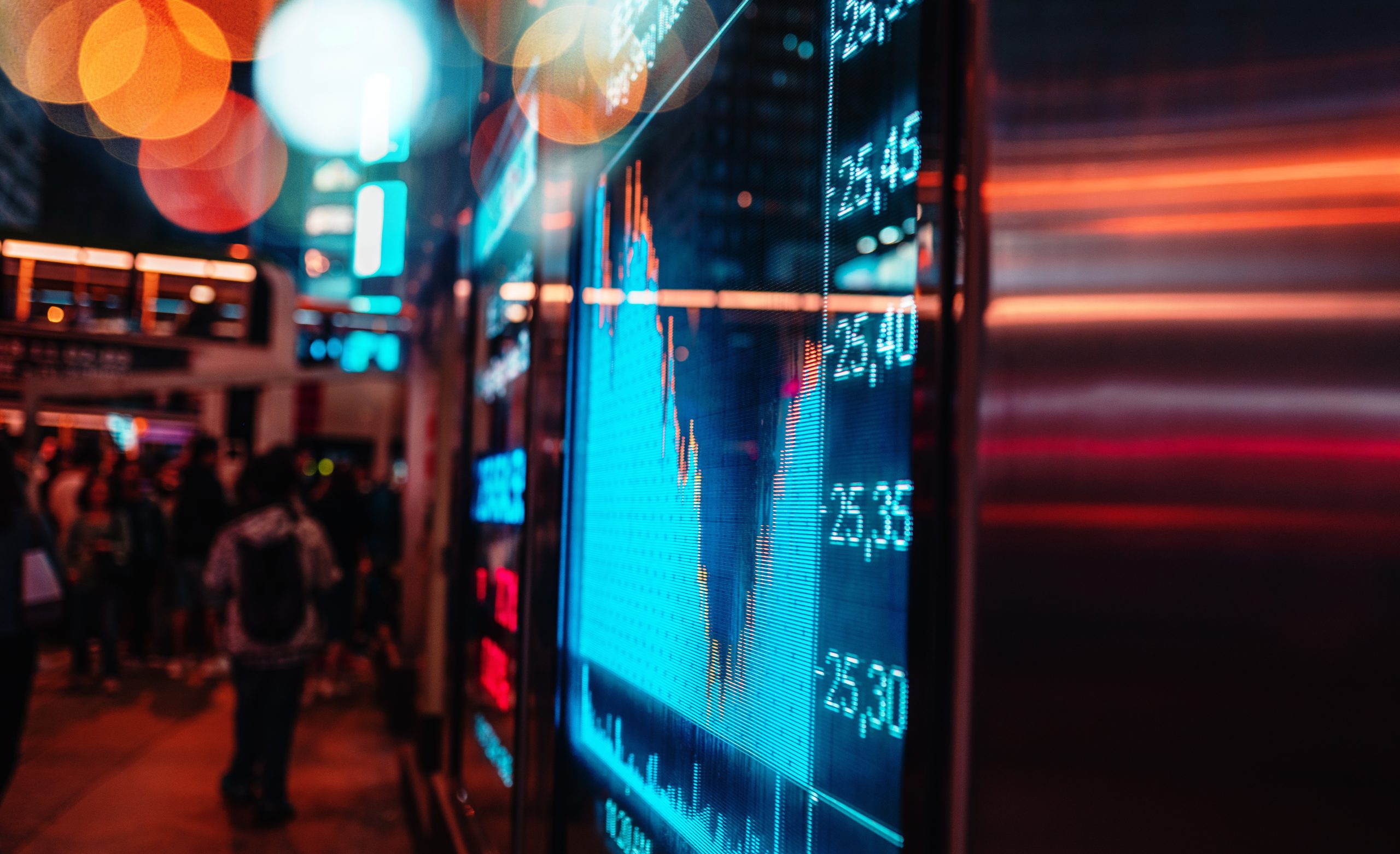 People walking past an LED display of stock prices